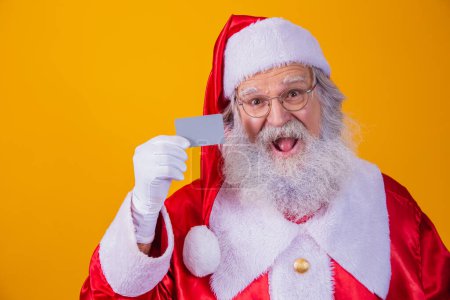 Téléchargez les photos : Photo du Père Noël tenant une carte de crédit sur fond jaune. Concept de paiement facile avec carte de crédit ou de débit. paiement bancaire - en image libre de droit