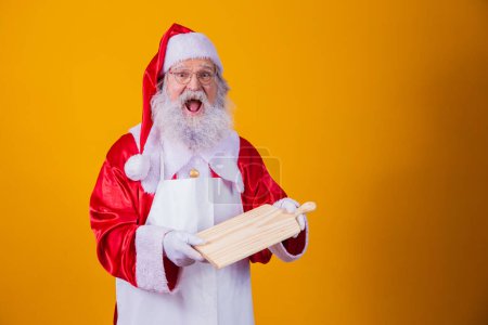 Téléchargez les photos : Père Noël vêtu d'un tablier contenant du carton de viande vide sur fond jaune. - en image libre de droit