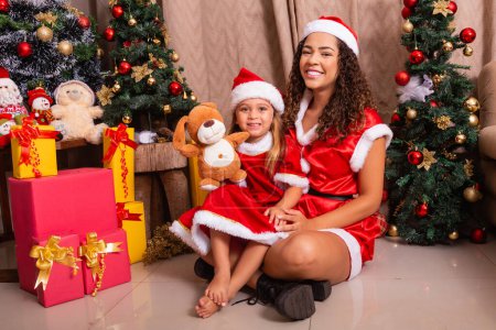 Photo for Young afro mother woman with daughter without lap dressed for christmas night at home. Mother and daughter sitting in christmas decoration. Merry Christmas - Royalty Free Image