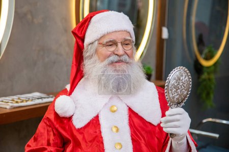 Photo for Real Santa Claus in the barbershop holding a mirror looking at himself. - Royalty Free Image