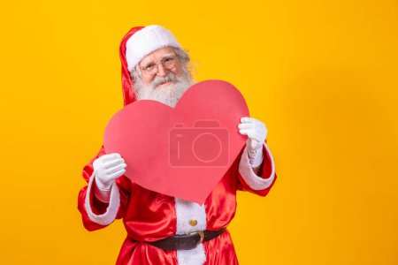Téléchargez les photos : Père Noël tenant grand carton rouge coeur en arrière-plan jaune. Père Noël romantique. - en image libre de droit