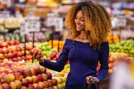 Photo for Young afro woman in supermarket buying apples. - Royalty Free Image