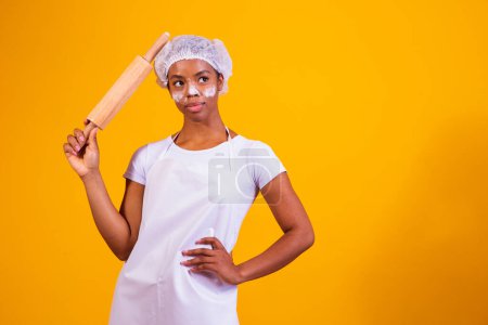 Photo for Young girl pizza maker on yellow background holding rolling pin. - Royalty Free Image
