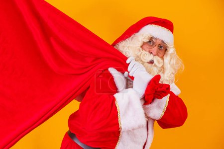 Photo for Santa Claus on yellow background holding bag with gifts with free space for text behind his back. christmas campaigns - Royalty Free Image
