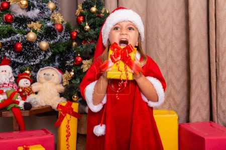 Foto de Linda niña caucásica vestida para Navidad en casa sosteniendo un regalo. - Imagen libre de derechos