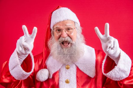 Photo for Santa Claus looking at the camera. Christmas is coming. Merry Christmas. Peace. V sign. - Royalty Free Image
