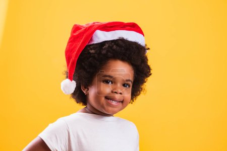 Téléchargez les photos : Petite fille afro enfant avec le chapeau du Père Noël souriant à la caméra - en image libre de droit