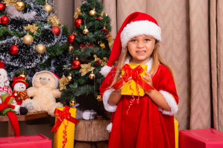 Foto de Linda niña caucásica vestida para Navidad en casa sosteniendo un regalo. - Imagen libre de derechos
