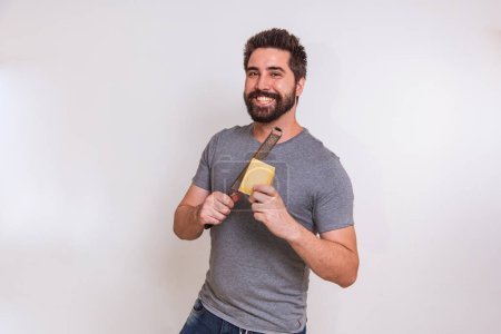 Téléchargez les photos : Jeune homme tenant une râpe et un morceau de fromage à la main sur fond gris. l'homme va râper le fromage - en image libre de droit