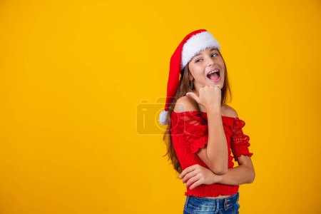 Photo for Little girl dressed for christmas pointing with her thumb on free space for text. Year-end promotion and campaigns - Royalty Free Image