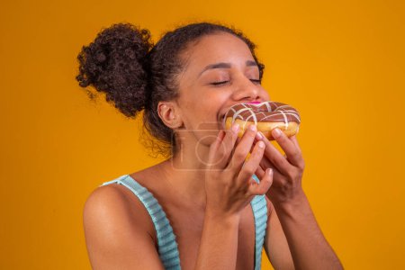 Photo for Young afro woman eating delicious chocolate donuts. - Royalty Free Image