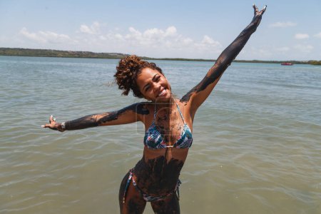 Téléchargez les photos : Jeune femme afro se baignant dans l'argile naturelle dans la rivière. - en image libre de droit