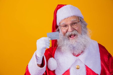 Téléchargez les photos : Photo du Père Noël tenant une carte de crédit sur fond jaune. Concept de paiement facile avec carte de crédit ou de débit. paiement bancaire - en image libre de droit