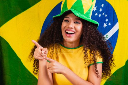 Téléchargez les photos : Femme noire fan. Brésil couleurs en arrière-plan, vert, bleu et jaune. Élections, football ou politique. - en image libre de droit
