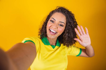 Foto de Apoyador de Brasil. Aficionada brasileña celebrando en el fútbol, partido de fútbol sobre fondo amarillo. Colores de Brasil. Smartphone selfie. - Imagen libre de derechos