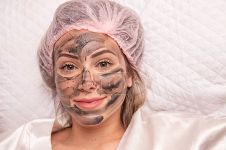 Photo for Woman is lying in the cosmetologist s office on the procedure of moisturizing her face. The cosmetologist applies a moisturizing mask to the patient's face. - Royalty Free Image