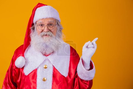 Téléchargez les photos : Drôle heureux excité vieux visage barbu Père Noël portant costume regardant caméra montrant pointant du doigt la publicité promotion de Noël, Nouvel An Noël rabais ad isolé sur jaune - en image libre de droit