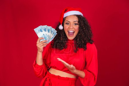 Photo for Afro woman counting Brazilian money bills. Real notes. 100 reais bills. Savings concept for the end of the year. Spend the Christmas. Spent on Christmas gifts. - Royalty Free Image