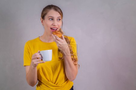Téléchargez les photos : Jeune femme caucasienne boire le thé de l'après-midi et manger des beignets - en image libre de droit