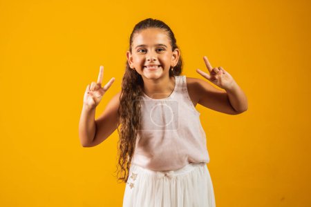 Photo for Adorable little girl making v sign on yellow background. good vibe peace and love - Royalty Free Image