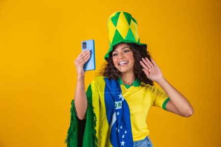 Photo for Brazil supporter. Brazilian woman fan celebrating on soccer, football match on yellow background. Brazil colors. Selfie smartphone. - Royalty Free Image