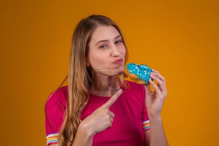Foto de Retrato de una joven rubia comiendo una deliciosa rosquilla colorida. - Imagen libre de derechos