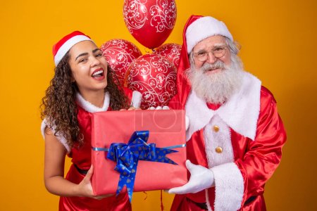Téléchargez les photos : Le vrai Père Noël avec son assistant noelete tenant le cadeau de Noël de l'enfant - en image libre de droit