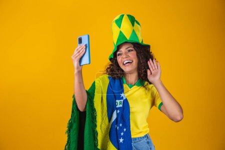 Foto de Apoyador de Brasil. Aficionada brasileña celebrando en el fútbol, partido de fútbol sobre fondo amarillo. Colores de Brasil. Smartphone selfie. - Imagen libre de derechos