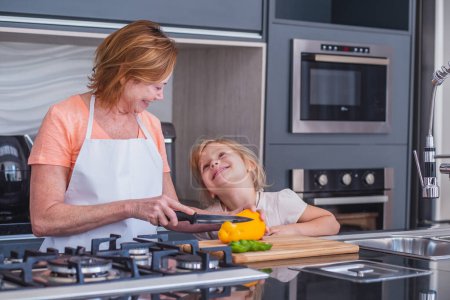Photo for Elderly mother and little daughter cooking together. Mother and daughter cutting vegetables for cooking - Royalty Free Image