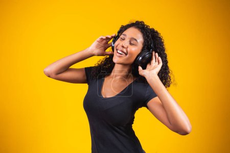 Young african woman wearing headphones on yellow background