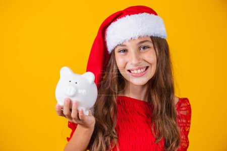 Photo for Smiling little girl with christmas hat holding piggy bank - Royalty Free Image