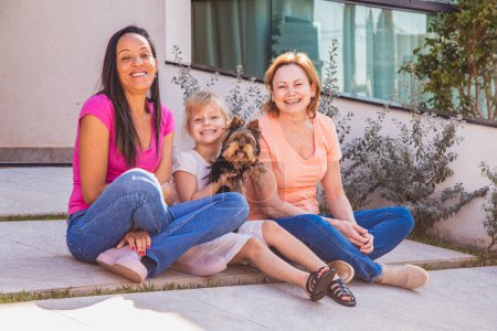 Photo for Smiling lesbian couple with child and pet puppy. Lesbian couple holding with their adoptive daughter, adoption concept. - Royalty Free Image