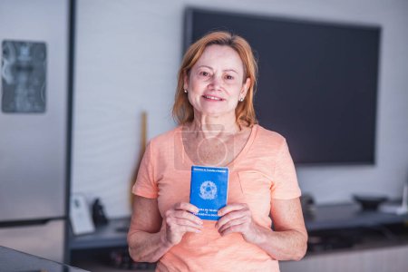 Téléchargez les photos : Travailleuse âgée tenant la carte de travail brésilienne en main. Femme âgée titulaire d'une carte de travail brésilienne - en image libre de droit