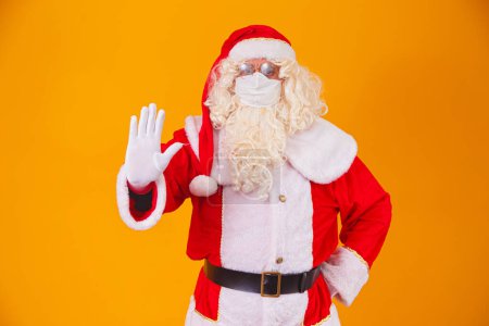 Téléchargez les photos : Véritable Père Noël sur fond jaune, portant un masque de protection contre la covid19. Noël avec distance sociale. Covid-19 - en image libre de droit