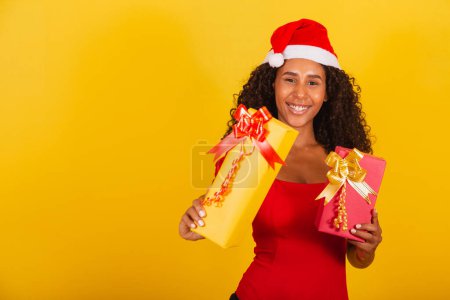 Photo for Beautiful black woman in santa claus hat holding merry christmas gift on yellow background. - Royalty Free Image