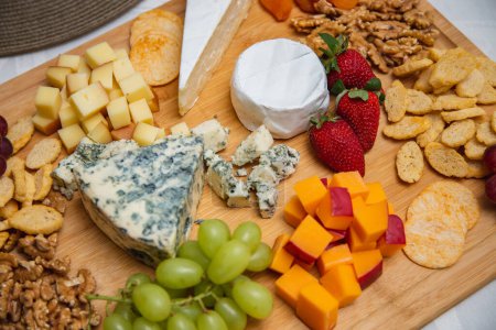 Foto de Plato de queso con variedad de aperitivos en la mesa. Platos de fresa, albaricoque, uva y queso de grano sobre la mesa - Imagen libre de derechos