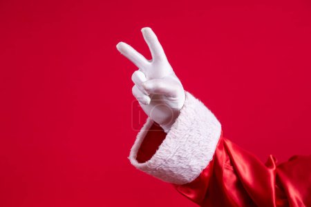 Photo for Close-up of Santa's gloved hand making v sign on red background. - Royalty Free Image