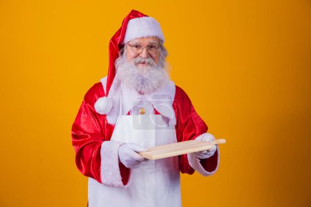 Foto de Santa Claus vestido con delantal sosteniendo cartón vacío sobre fondo amarillo. - Imagen libre de derechos