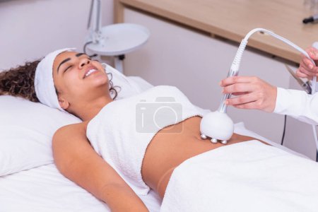 Photo for Cropped shot of a professional dermatologist performing radiofrequency lifting procedure on the stomach of a woman. Female client getting rf-lifting treatment on her belly at cosmetology clinic - Royalty Free Image