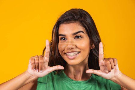 Téléchargez les photos : Jeune femme souriante faisant cadre photo avec les mains et les doigts avec un visage heureux. concept de créativité et photographie. - en image libre de droit