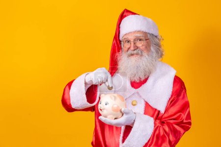 Téléchargez les photos : Le Père Noël met de la monnaie dans une tirelire en céramique. Concept d'épargne pour la fin de l'année. Je passe Noël. Passé sur les cadeaux de Noël
. - en image libre de droit