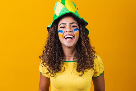 Foto de Apoyador brasileño. Aficionada brasileña celebrando en el fútbol o partido de fútbol sobre fondo amarillo con espacio de copia. Brasil colores. - Imagen libre de derechos