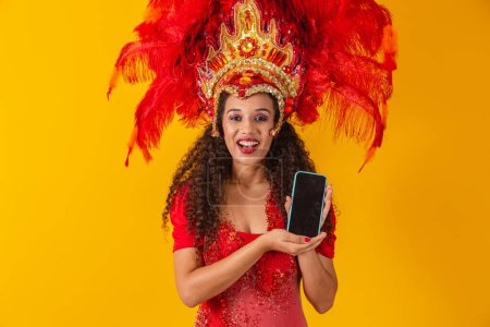 Foto de Hermosa joven con traje especial de plumas de carnaval sosteniendo un teléfono inteligente con pantalla en blanco con espacio para el texto. Carnaval virtual, promoción y publicidad. - Imagen libre de derechos