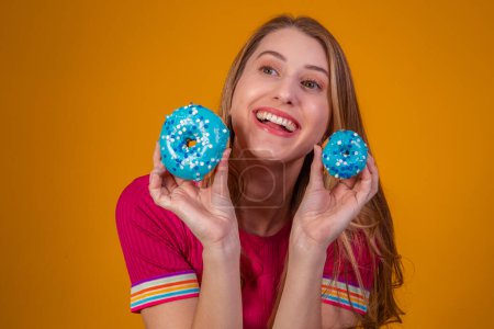 Téléchargez les photos : Portrait d'une jolie fille joyeuse tenant des beignets bleus à son visage - en image libre de droit