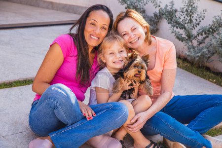 Foto de Pareja lesbiana sonriente con niño y cachorro de mascota. Pareja lesbiana sosteniendo con su hija adoptiva, concepto de adopción. - Imagen libre de derechos