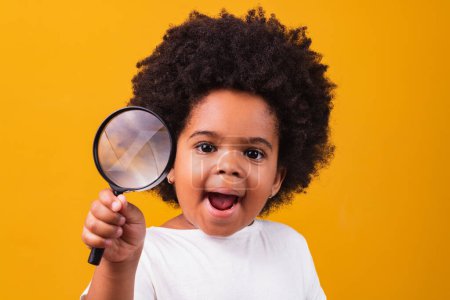 Téléchargez les photos : Enquête, découverte et concept de vision - heureuse petite afro-américaine regardant à travers la loupe sur fond jaune - en image libre de droit