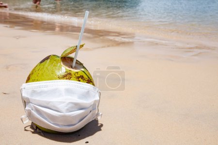 Photo for Photo of a coconut on the beach with surgical mask. Pandemic and vacation concept - Royalty Free Image