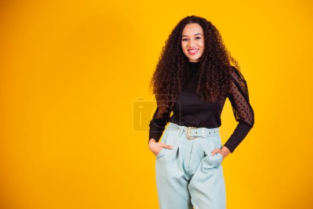 Photo for Beauty portrait of a Brazilian woman with afro hairstyle and glamour makeup. Latin woman. Mixed race. Curly hair. Hair style. Yellow background - Royalty Free Image