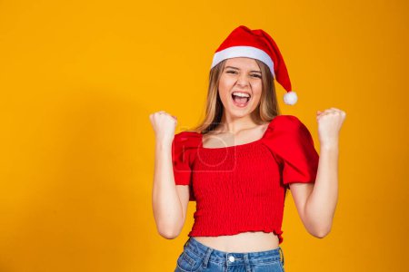 Foto de Chica rubia joven con sombrero de Navidad celebrando sorprendido y sorprendido por el éxito con los brazos levantados. concepto ganador. - Imagen libre de derechos
