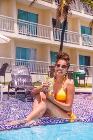 Photo for Young woman on vacation at the hotel swimming pool having a delicious alcoholic drink. - Royalty Free Image